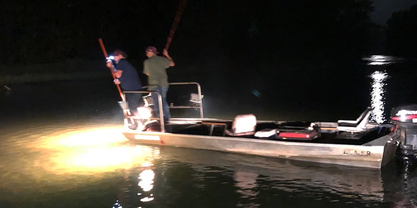Men fishing on a boat at night with the water lit up by flashlights